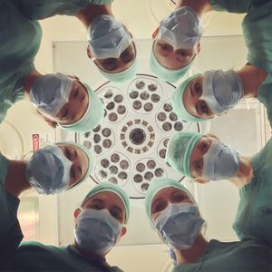 eight doctors, all masked, looking over a patient as seen from the patient's perspective
